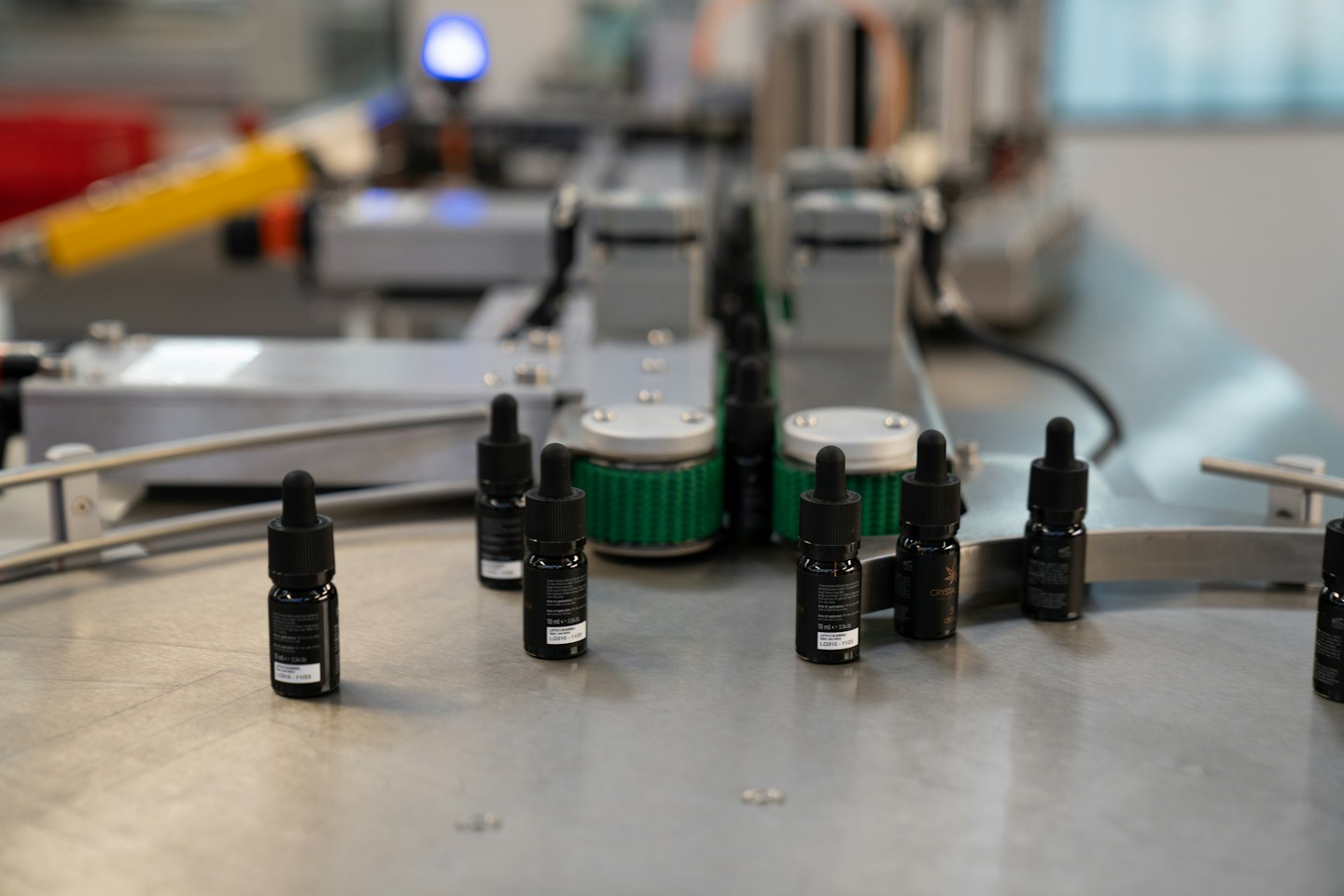Small black dropper bottles on a clean manufacturing conveyor belt.