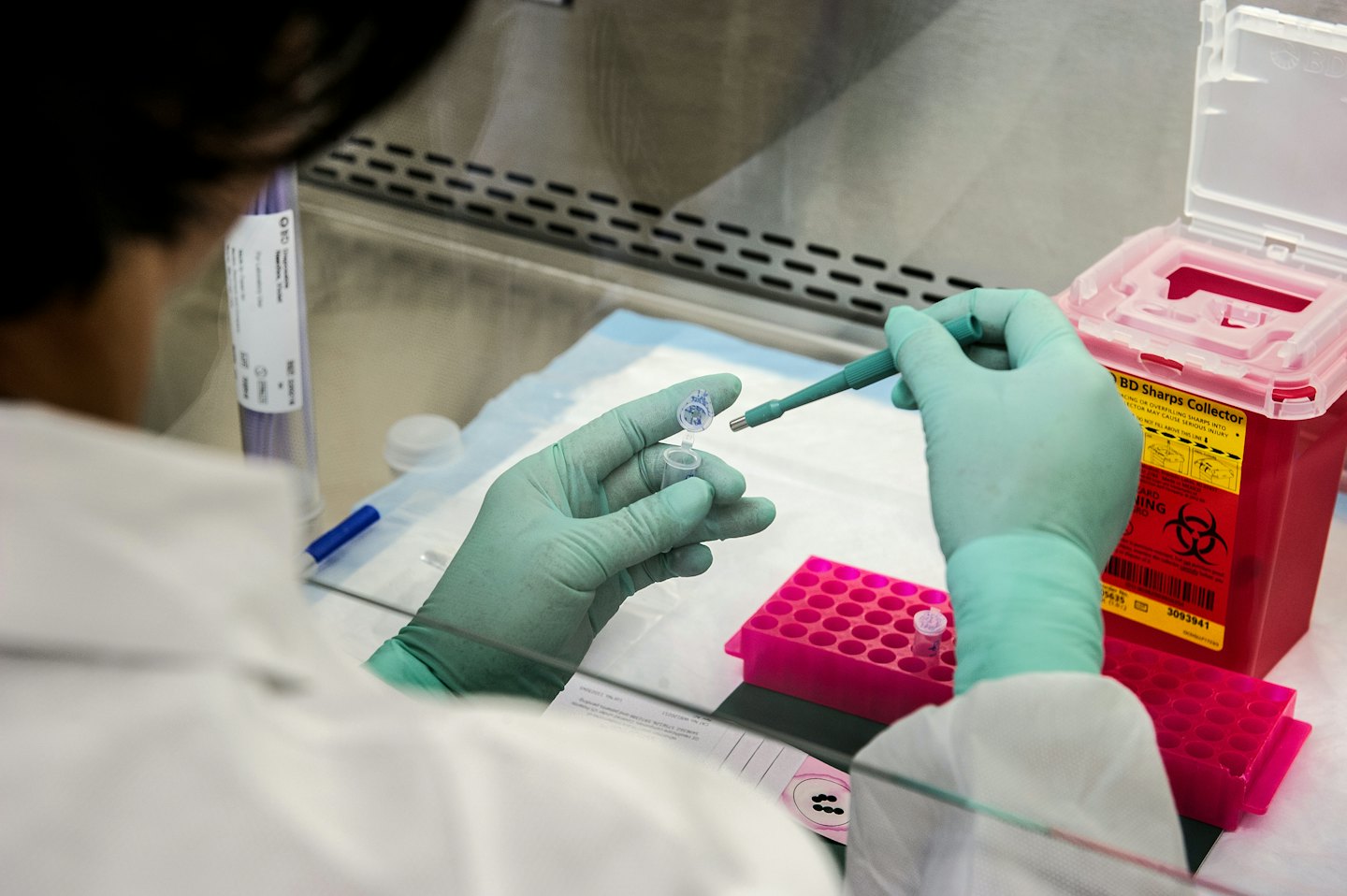 Lab technician in green gloves transfers sample to vial.
