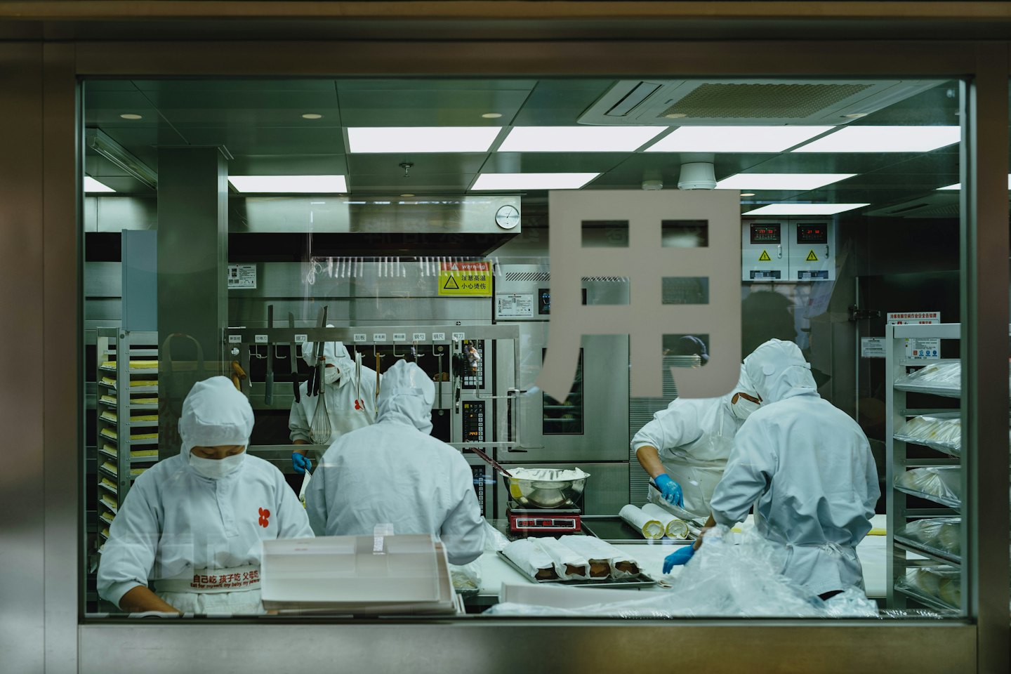 Workers in protective gear package food on stainless steel counters.