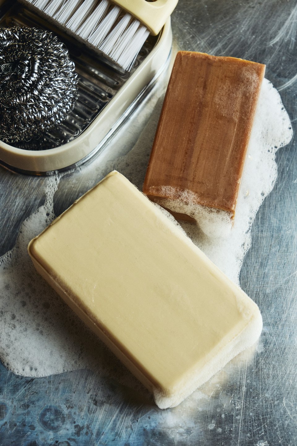 Two soap bars and a dish brush sit on sudsy metal.